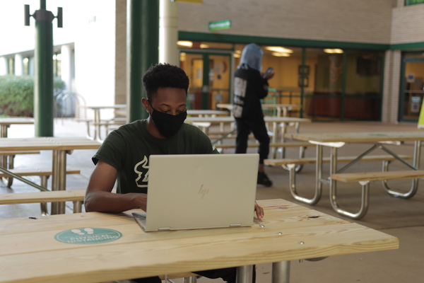 Student on laptop in breezeway of Student Services building