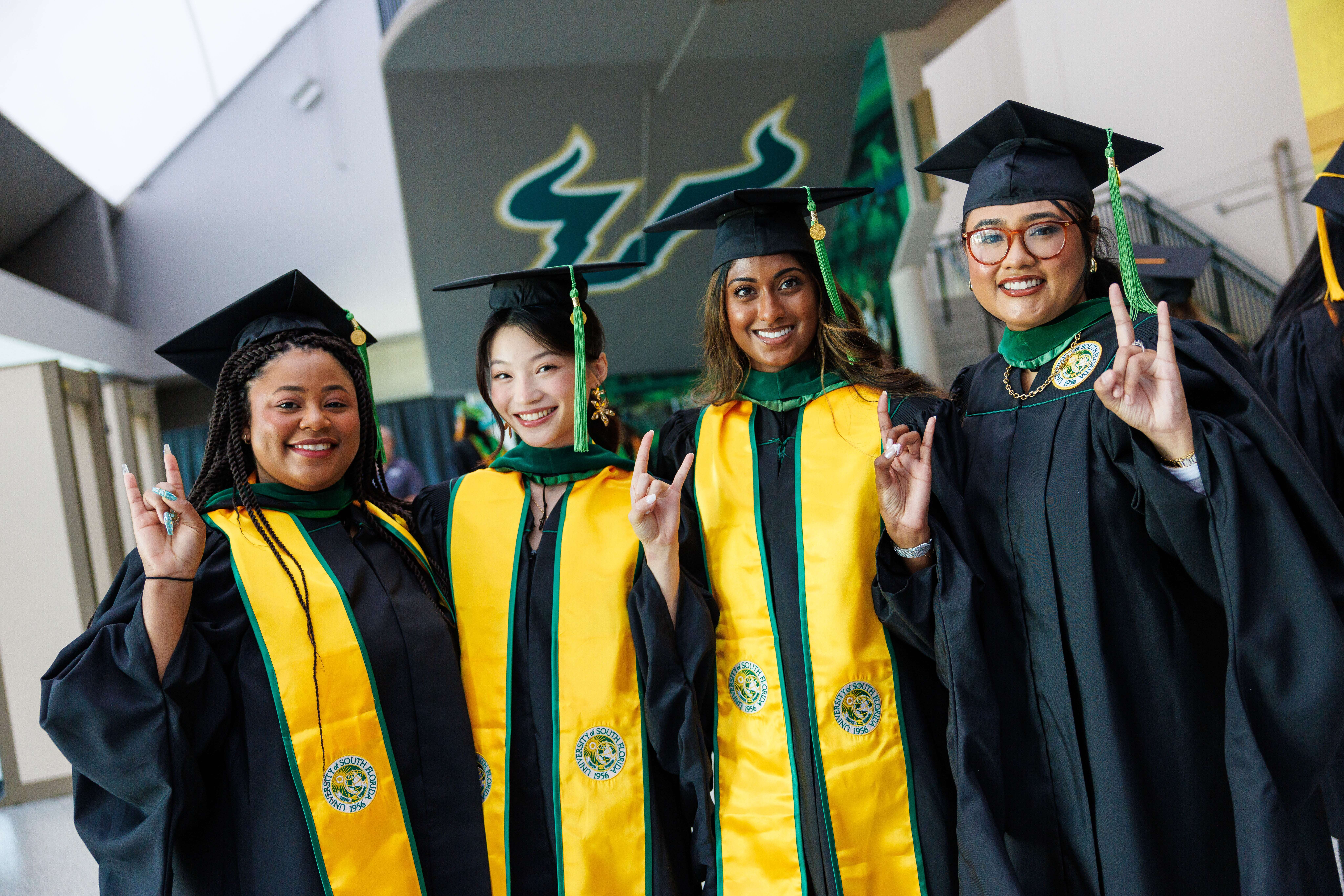 Three women in graduation regalia doing the Horns Up sign